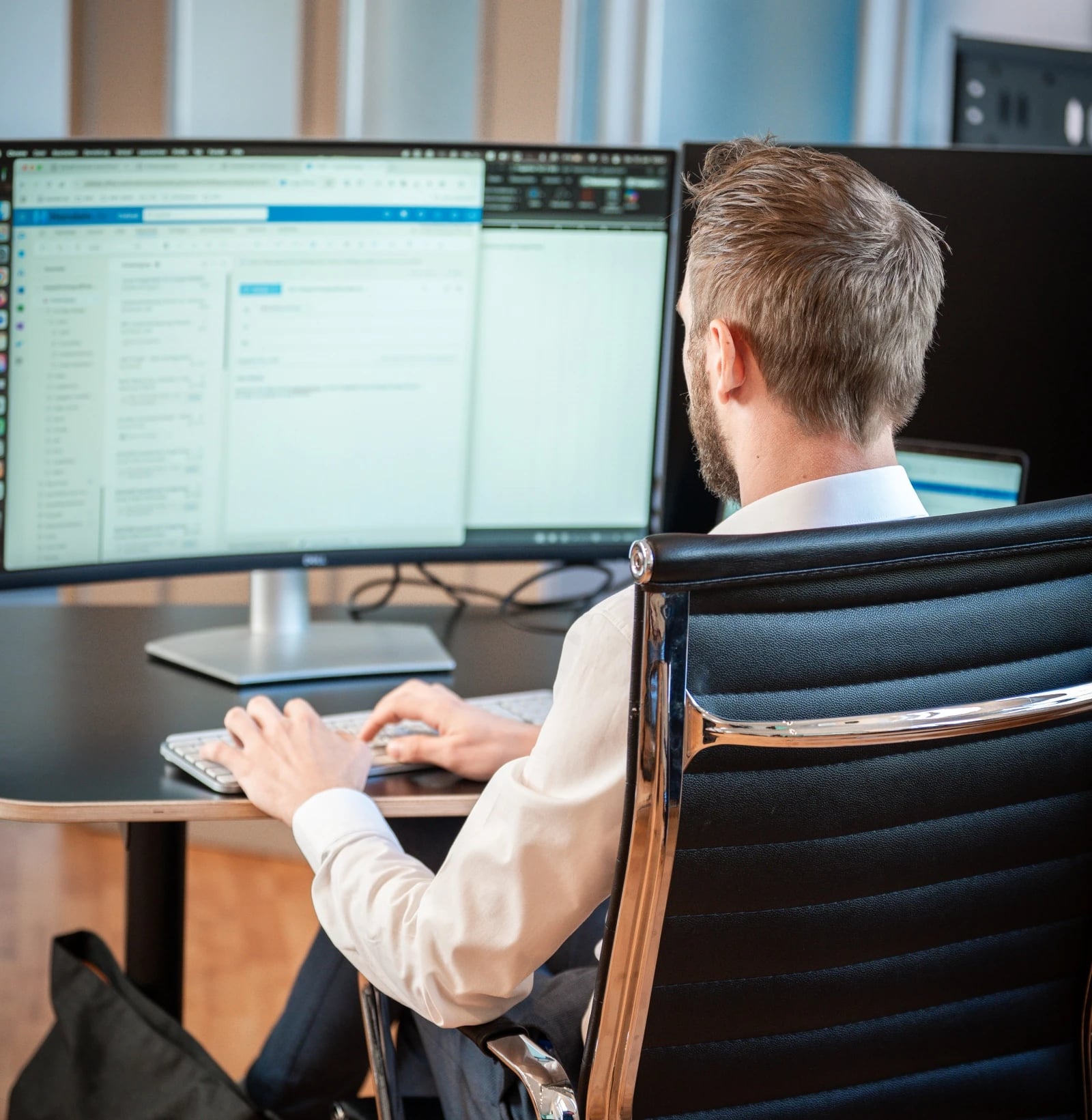 Mann arbeitet am Schreibtisch vor großem Monitor