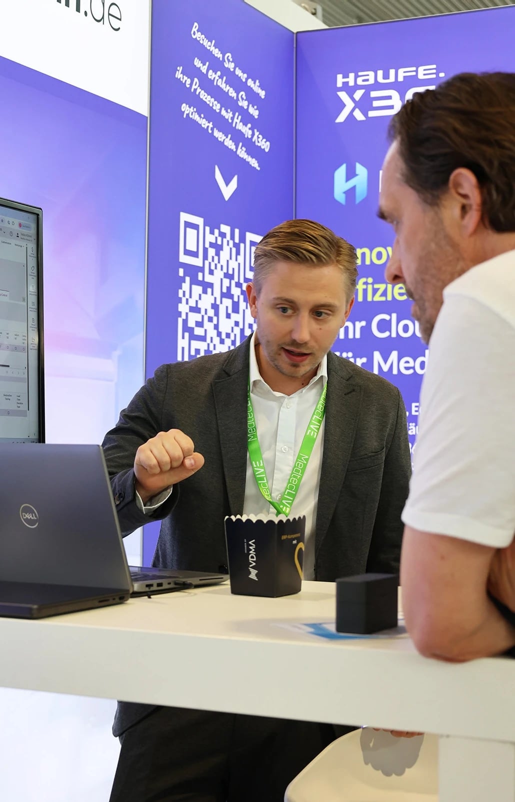 Beratungsgespräch am Messestand mit Laptop und QR-Code