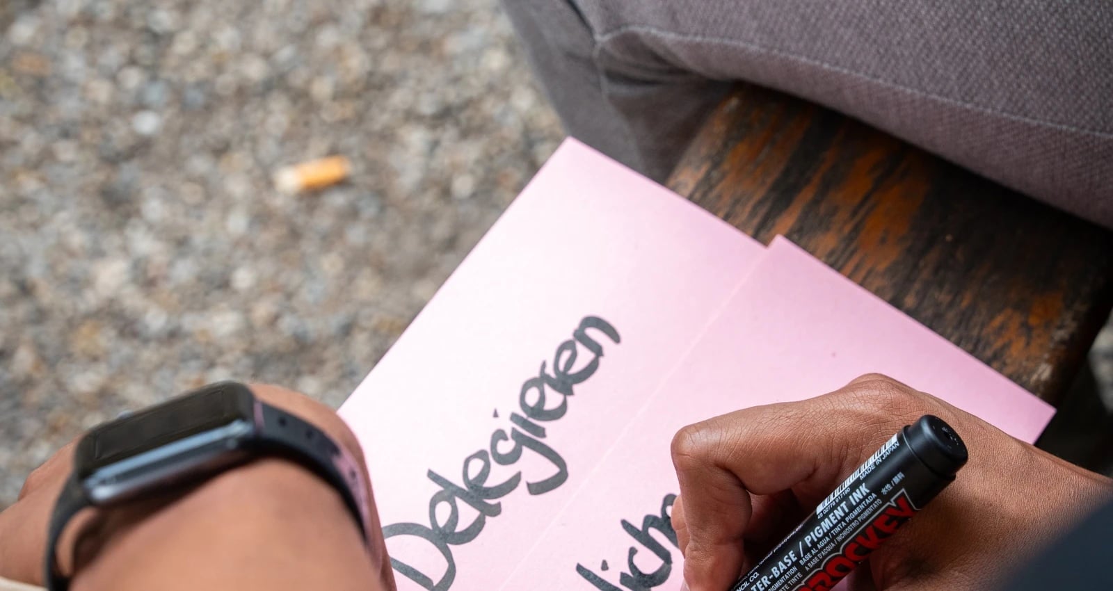Person schreibt „Designen“ auf rosa Papier